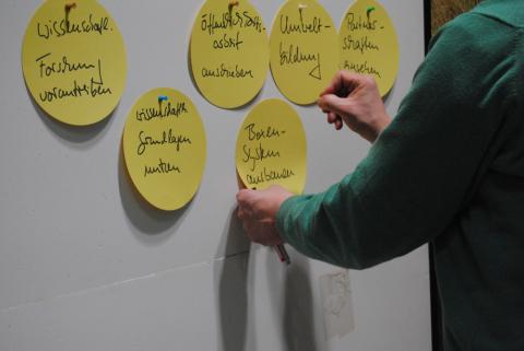 Nahaufnahme einer Pinnwand. Jemand heftet einen Beitrag an die Pinnwand. 